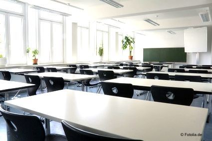 Ein leerer Schulungsraum mit hellen Tischen und schwarzen St&uuml;hlen. Aufstellung in drei Reihen mit jeweils mehreren Tischen hintereinander und jeweils zwei Sitzpl&auml;tzen.